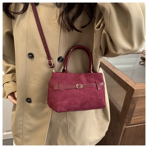 Détail du sac en daim bordeaux avec boucle dorée porté sur un trench-coat de couleur kaki