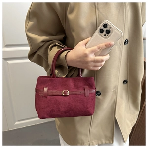 Détail d'un sac cabas en daim bordeaux avec boucle dorée et bordure en cuir sur trench