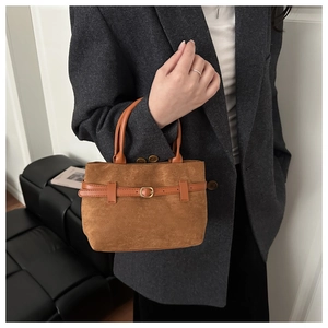 Close-up of brown suede tote bag featuring leather straps and golden metal buckle details