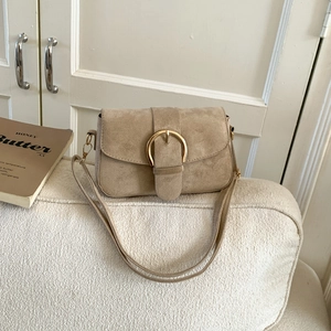Detail of tan suede crossbody bag featuring a large decorative gold round metal buckle