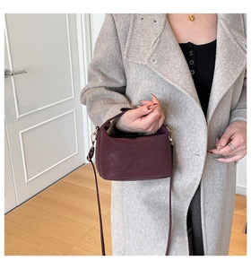 Detail view of a vintage deep purple crossbody bag with golden hardware on wool coat