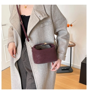 Detail of a vintage burgundy leather doctor bag with a gold clasp worn by a model