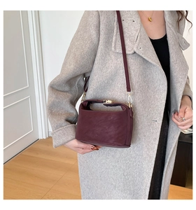 Model wearing wine red leather crossbody pillow bag with elegant gold hardware detail