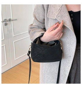 Detail of a black mini crossbody bag in matte leather worn by a model in a minimal setting