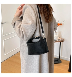 Detail view of a black matte crossbody bag with gold hardware worn by a model