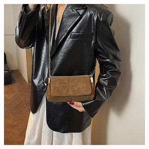 Close-up of brown suede crossbody bag with gold chain strap worn over black blazer