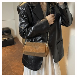 Détail d'un sac bandoulière en daim marron avec surpiqûres et chaîne dorée