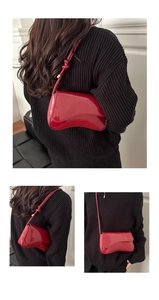 Close-up of deep red glossy patent leather shoulder bag with wavy flap design and knot strap