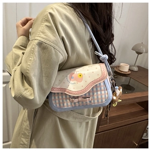 Detail of blue plaid crossbody bag featuring cartoon print and cute bear pendant charm