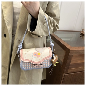 Detail of blue plaid saddle bag with pink bow, bear charm, and heart pattern print