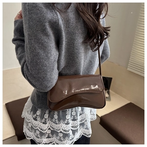 Detailed back view of a glossy coffee brown patent leather shoulder bag on a model