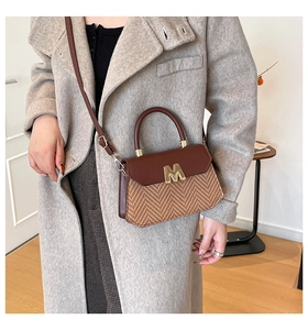 Detail van een vintage gestreepte crossbodytas met gouden M-logo op een grijze jas