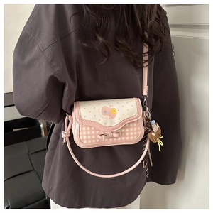 On-body view of a pink cartoon embroidered crossbody bag with a plush bear charm