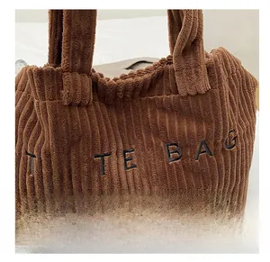 Close-up van bruine corduroy stofstructuur en geborduurde TOTE BAG tekst op een schoudertas