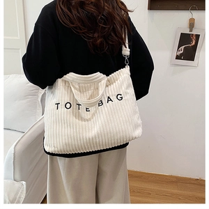 Detailweergave van de gebroken witte corduroy tote bag met zwarte letters op de brede schouderriem