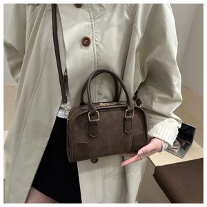 Dettaglio borsa Boston marrone con goffratura QTN indossata su un trench coat beige