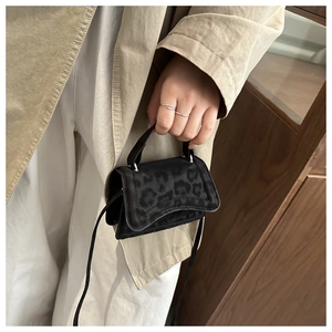 Dettaglio di una mini borsa leopardata nera con manico superiore e tracolla sottile
