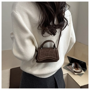 Dettaglio mini borsa a tracolla marrone scuro con fondo curvo su maglione bianco