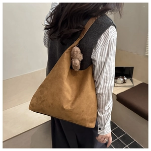 Dettaglio di una borsa tote in pelle scamosciata marrone con ciondolo a forma di orso per pendolari
