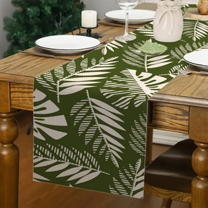 Detail van linnen tafelloper met tropisch groen en wit bladpatroon op houten tafel