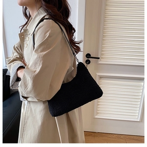 Detail of a black plush lamb-wool underarm bag styled with a trench coat in a cozy room