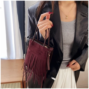 Dettaglio di una borsa in camoscio bordeaux con frange mostrata in un contesto lifestyle