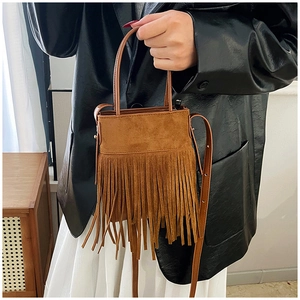 Dettaglio borsa in camoscio marrone con frange lunghe, indossata da una modella elegante
