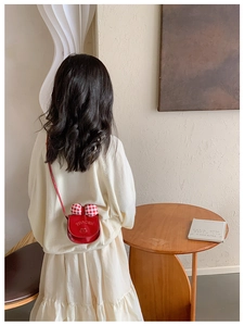 Detail view of a red patent leather kids purse with a checkered bow and cat motif