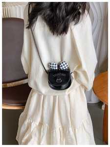 Close-up of kids crossbody bag with black gloss finish and plaid bow on beige sweater