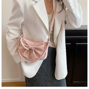 Dettaglio borsa rosa con fiocco, catena di perle e tracolla in pelle testurizzata