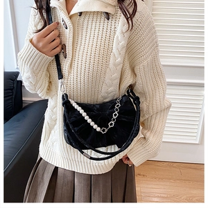 Dettaglio borsa a mezzaluna in velluto nero con catena di perle su maglione beige