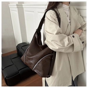 Dettaglio borsa tote marrone scuro con zip argentate indossata a spalla dal modello