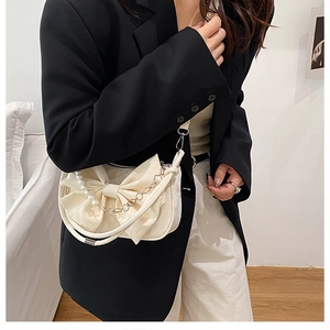 Elegante borsa a tracolla color crema con fiocco e perle su blazer nero