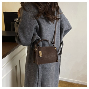 Detail of dark brown leather handbag with gold buckle shown on a model in a minimal setting