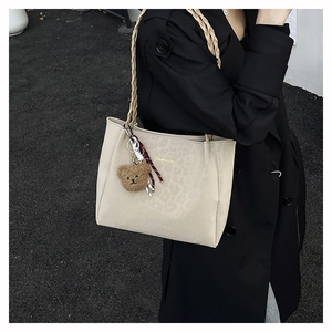Dettaglio della borsa tote leopardata beige con manici intrecciati e ciondolo a orsetto