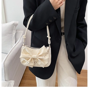Dettaglio borsa crema con fiocco, catena di perle e tracolla in metallo elegante