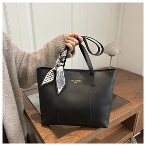 Dettaglio borsa tote in pelle nera con logo dorato e foulard di seta con motivi geometrici