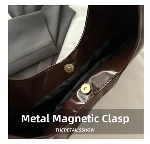 Dettaglio della chiusura magnetica dorata sulla borsa in pelle marrone lucida