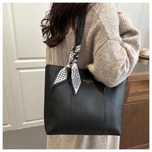 Dettaglio della borsa tote nera con scritte dorate e sciarpa di seta blu a motivi geometrici