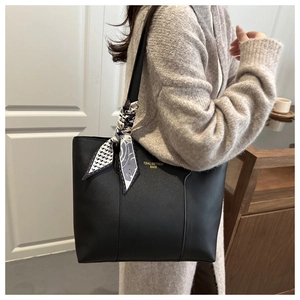 Dettaglio di una borsa tote in pelle nera con un foulard decorativo fantasia sul manico