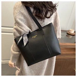 Dettaglio borsa tote in pelle nera con foulard di seta e logo dorato portata a spalla