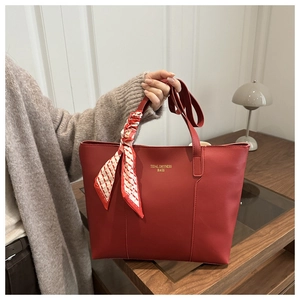 Dettaglio della borsa tote in pelle bordeaux con foulard di seta e logo dorato