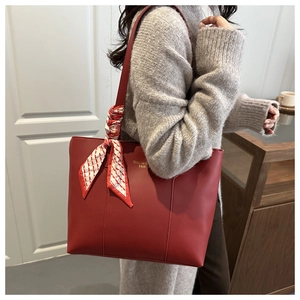 Dettaglio della borsa tote in pelle rossa con sciarpa di seta a quadretti sul manico