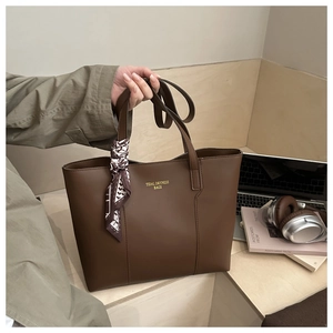 Dettaglio della borsa tote in pelle marrone scuro con logo dorato e accessorio foulard in seta