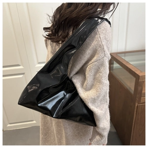 Vista a spalla della borsa tote grande in pelle verniciata nera lucida su un modello