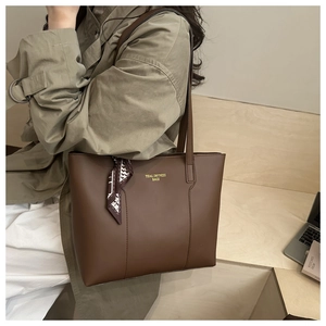 Dettaglio di una borsa tote in pelle marrone con un foulard di seta legato al manico