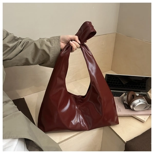 Dettaglio della borsa in pelle lucida rosso scuro con un design unico del manico annodato