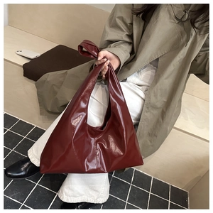 Dettaglio di una grande borsa a spalla bordeaux lucida abbinata a un outfit con trench