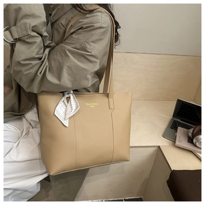 Dettaglio di una borsa tote beige capiente con foulard decorativo e scritte dorate sulla pelle
