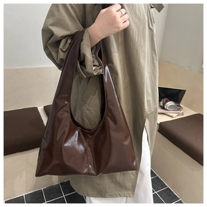 Dettaglio di una borsa tote marrone scuro lucida indossata da una modella